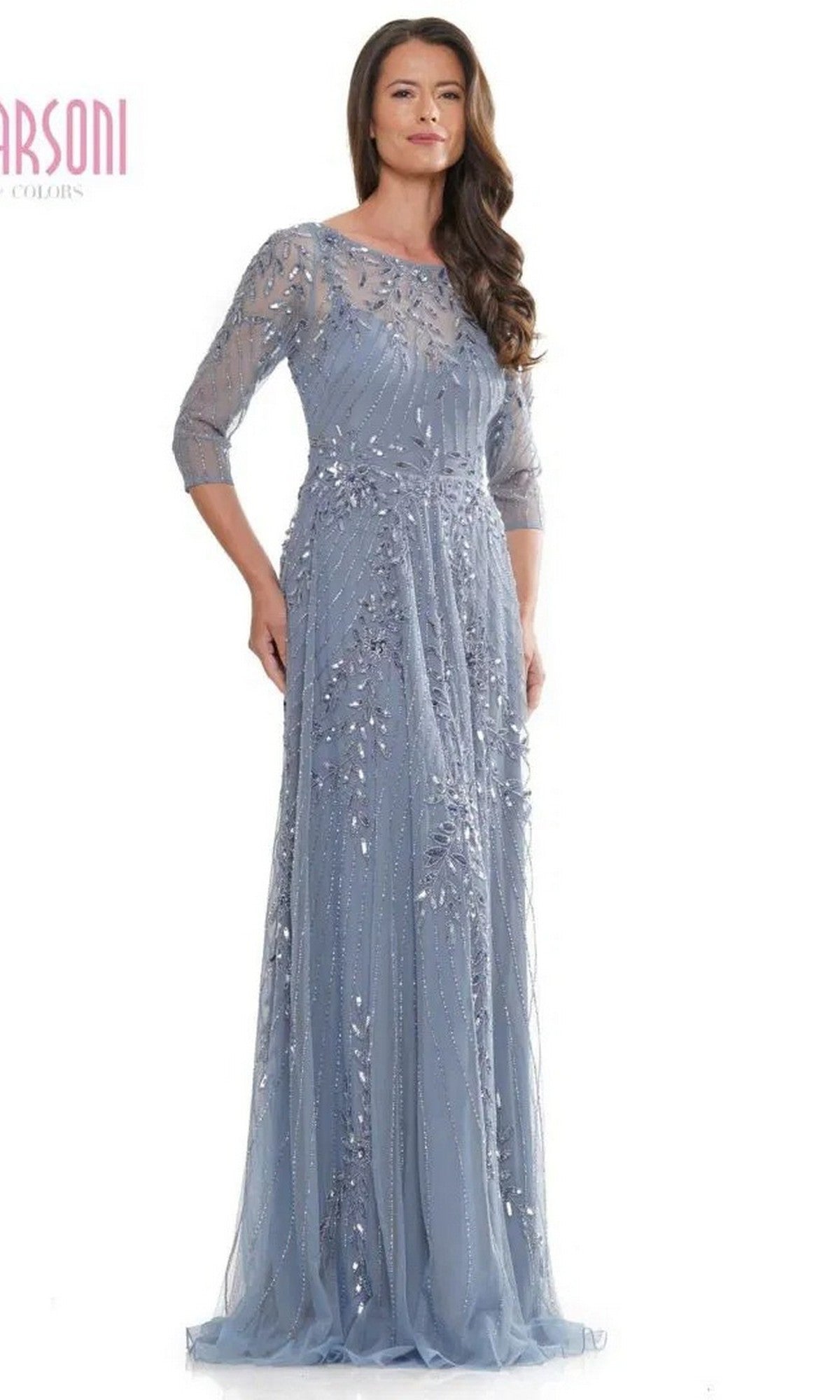 A woman wears the Marsoni MV1283 long formal dress in slate blue, featuring sheer sleeves and detailed sequin embellishments—an elegant choice for a mother of the bride—while standing against a plain background.